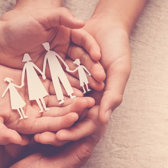 Adult and children hands holding paper family cutout, family hom