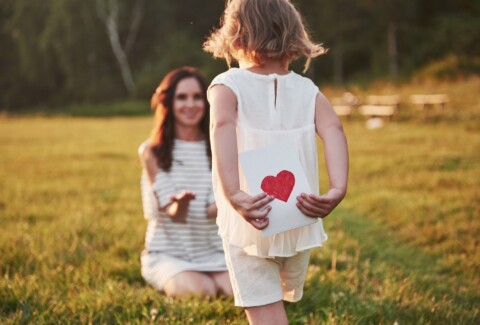The child's daughter congratulates her mother and gives her a postcard. Mother and girl smile and hug.
